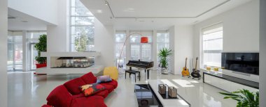 Lüks özel evin modern iç mimarisi. Geniş oturma odası, kırmızı kanepe, piyano, beyaz masa..