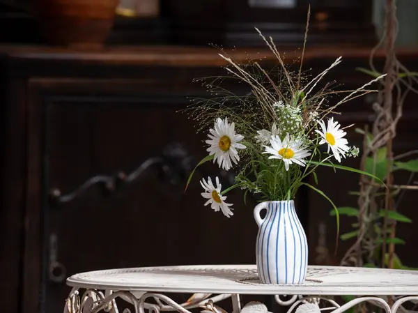 Close-up of daisies in a vase on table. Wooden furniture in background