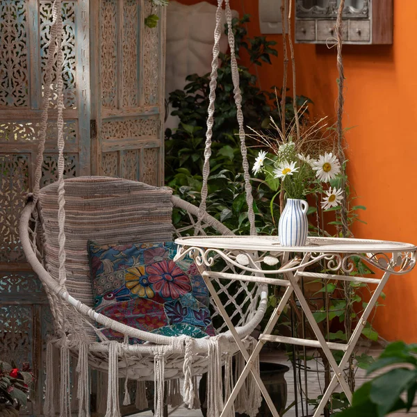 Interior of veranda. Hanging wicker chair, flowers on table. Close-up.