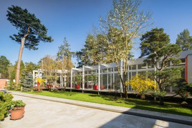 Lüks özel evin modern dış cephesi. Güneşli bir yaz günü. Cam duvar. Bahçedeki güzel ağaçlar.