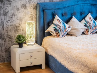 Yatak odasının modern iç mekanı. Beyaz komodinin üzerinde yanan lambanın yakın çekimi. Ev dekoru. Yeşil bitki.