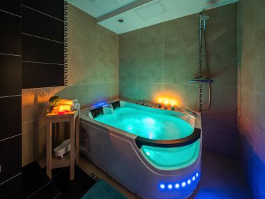 Lüks banyonun modern iç mekanı. Suyla aydınlatılmış masaj banyosu. Mumlar. Romantik atmosfer.