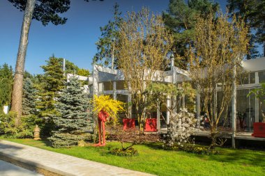 Lüks özel evin modern dış cephesi. Güneşli bir yaz günü. Cam duvar. Bahçedeki güzel ağaçlar.