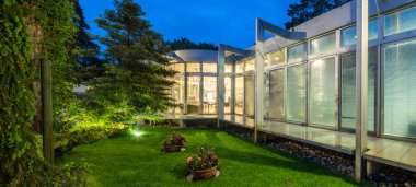 Alacakaranlık 'taki lüks özel evin modern dış cephesi. Güzel yeşil bahçe. Cam duvar..