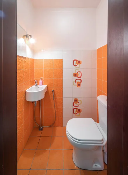 Modern interior of small bathroom. Orange tile. Sink and toilet.