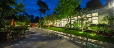 Alacakaranlık 'taki lüks özel evin modern dış cephesi. Güzel yeşil bahçe. Cam duvar..