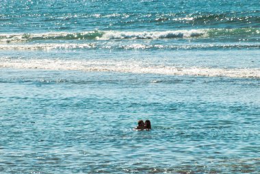 Endonezya 'nın Bali Adası, Canggu sahilinin önündeki hindistan cevizi denizinde yüzen genç çift..