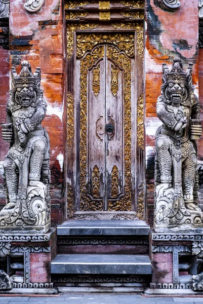 stock image Ancient carved wooden door protected by two stone statues of Gods in Tirta Empul temple near Ubud, Indonesia, Bali 