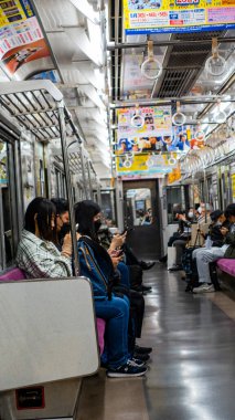 Japonya, Nisan 2024: Çevredeki yolcuların çatıdan sarkan renkli reklam tabelaları, Japonya.