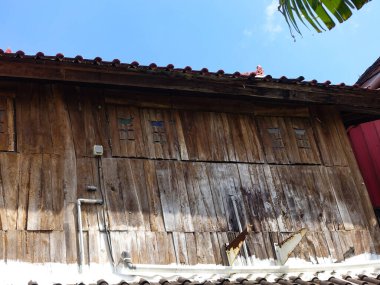 Kırsal ahşap dikiş evi, iki kepenk kapalı, dikey parmaklıkları ortaya çıkarıyor. Pencere, Canggu, Bali, Endonezya 'da geleneksel bir stilt evi olan yıpranmış ahşap bir duvara kurulmuş. Temmuz 2025.