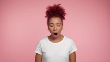 Portre, Afro-Amerikan kıvırcık saçlı kadının kameraya ağzı açık bakmasına şok oldu. Beyaz tişörtlü, izole edilmiş pembe arka planda fotokopi alanı olan heyecanlı bir kadın. İnsanların duyguları yaşam tarzı