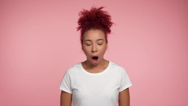 ポートレートはアフリカ系アメリカ人の赤毛の女性が口を開けてカメラを見てショックを与えた コピースペースと隔離されたピンクの背景に立つ白いTシャツの興奮した女性 人々の感情ライフスタイル — ストック動画