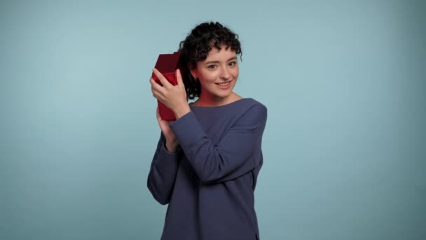 Hermosa Mujer Rizada Sonriente Sacudiendo Regalo Envuelto Caja Roja Cerca — Vídeo de stock