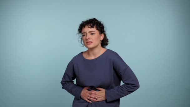 不健康的卷曲女人摸着胃感到不适或疼痛 因疼痛 胃炎或孤立的浅蓝色背景下便秘而愁眉苦脸的女性病人 — 图库视频影像
