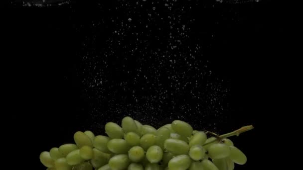 黒い背景に透明な水に落ちる遅い動きの緑のブドウ 水族館で新鮮な果物が飛び散る 健康食品 — ストック動画