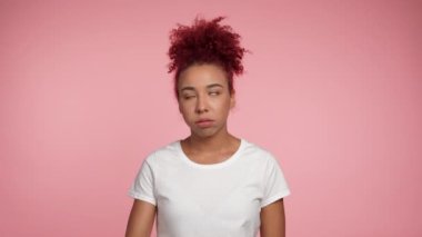 Portrait disappointed African American redhead curly woman face palm shaking head touching face in despair looking camera. Female in white t-shirt standing on isolated pink background with copy space