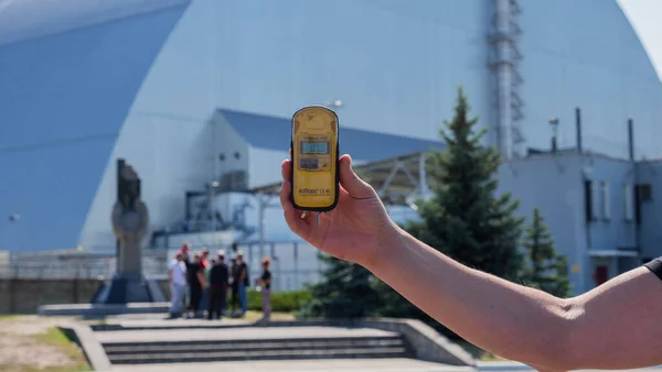 排拒区 乌克兰 Pripyat 2019年8月26日 在新的安全石棺下 背景第四反应堆切尔诺贝利核电厂的剂量计在手 切尔诺贝利事故的清算人纪念碑 — 图库照片