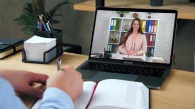 Bilgisayar ekranı konuşmasında kadın öğretmenlik yapıyor. Öğrencilere uzaktan giysi kursu dersi veriyor. Uzaktan eğitim. Ev ofisteki adam video çalışıyor webcam chat laptop öğretmeni, deftere yazıyor.