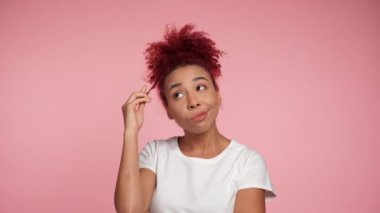 Düşünceli, gülümseyen, beyaz tişörtlü, kıvırcık saçlı Afro-Amerikan kadın, düşünmekten kaçınıyor. Pembe arka planda fotokopi aletiyle duran düşünceli, pozitif kadın.