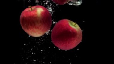 Slow motion three red apple falling into transparent water on black background. Beautiful fresh fruit splashing in aquarium. Organic fruits, healthy food, diet, air bubbles