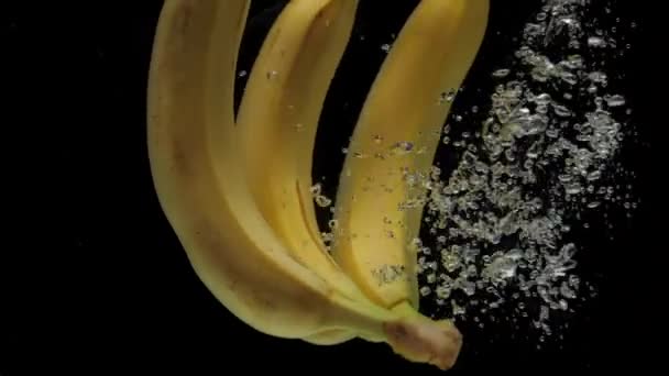 缓慢运动的香蕉在黑色的背景上掉进透明的水里 新鲜水果洒在水族馆里 健康食品 — 图库视频影像