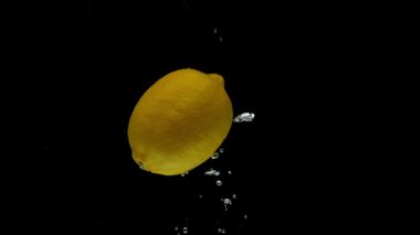 Yavaş çekimde bir sarı limon siyah arkaplanda şeffaf suya düşüyor. Akvaryuma taze meyve sıçraması. Citrus, yemek, hava kabarcıkları