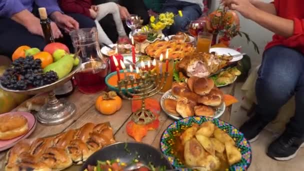幸せなユダヤ人の家族はハヌカの休日を祝う ハヌカは家族や友人と家でライトを灯します Chankahテーブルディナーや食品 前景に9本のロウソクが灯るメノア — ストック動画