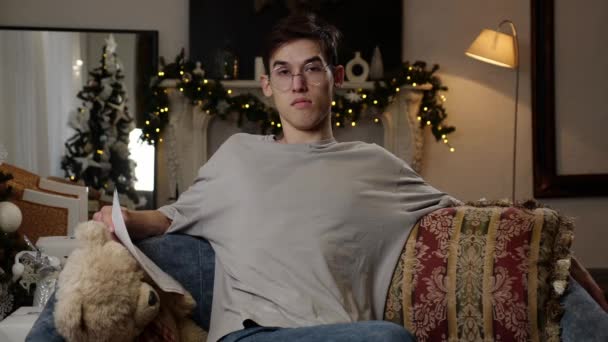 紙を持つ美しいロマンチックな若者は クリスマスツリーとライトで装飾されたリビングルームのソファーに座っています 高品質の4K映像 — ストック動画
