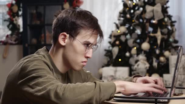 若い男性はクリスマス休暇中に自宅でコンピュータで一生懸命働いています 高品質の4K映像 — ストック動画