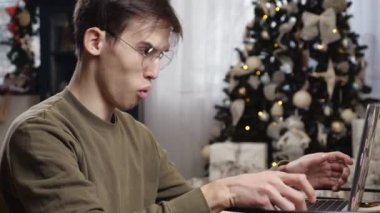 Genç bir adam Noel tatilinde evde video bağlantısıyla konuşur. Şaşkınlık ve öfke duygusu. Yüksek kalite 4k görüntü