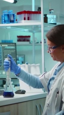 Dikey video: Bilimadamı kadın pipet sıvısını gece geç saatlerde modern laboratuarda test etmek için kullanıyor. Ekip, tedavi gelişiminin bilimsel analizi için yüksek teknoloji kullanarak virüs evrimini inceliyor
