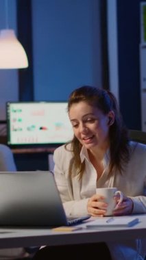 Dikey video: Müdür, gece geç saatlerde uzaktan iş arkadaşlarıyla çevrimiçi konuşuyor ve gece yarısı laptopun başındaki ofiste oturuyor. Sanal toplantıda kablosuz iletişim kullanan bir çalışan.