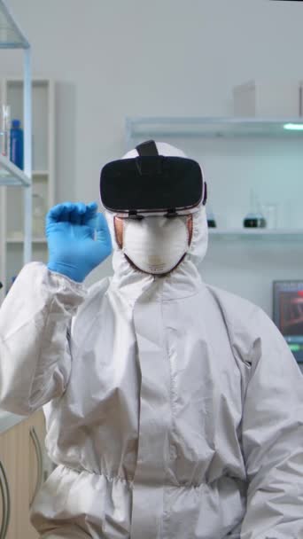 垂直ビデオ 化学実験室で働くVrを使用して保護スーツの研究者 高い技術と技術でワクチンの進化を調べる生物学者チーム — ストック動画