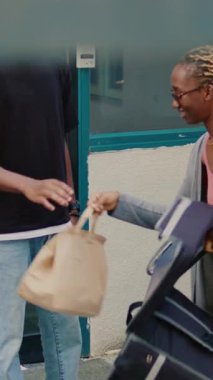 Dikey video: Afro-Amerikalı bir adam yemek siparişini ödemek için smartwatch nfc kullanıyor, kadın taşıyıcı fast food paketi veriyor ve postal terminalini tutuyor. Müşteri binadaki bağlantısız ödemeyi kullanıyor