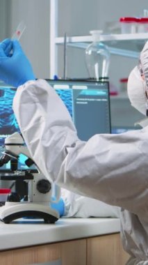 Dikey video: Kimya araştırmacısı, modern donanımlı laboratuardaki cam ekipmanlarından alınan bakteri örneklerine bakıyor. Aşı evrimini araştırmak için yüksek teknoloji kullanılıyor.