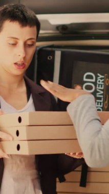Dikey video: Afrikalı Amerikalı teslimatçı araba bagajından paketleri alıyor, kadın müşterilere yığınla pizza veriyor. Fast food kuryesi kadınlara büyük pizza siparişi veriyor.