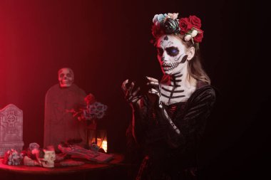 Santa Muerte modeli akıllı telefondan video oyunu oynuyor, Cadılar Bayramı kutlamalarında cep telefonu kullanıyor. La Cavalera Catrina kutsal Meksika festivalinde eğleniyor, ürpertici bir tatil..