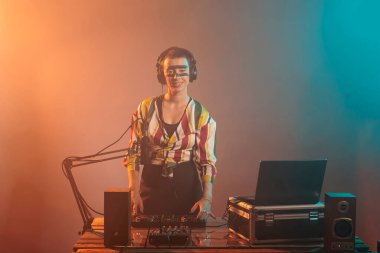 Havalı bir sanatçı pikaplarda müzik karıştırıyor, DJ müzik aleti ve ekipman kullanarak tekno müzik çalıyor. Çılgın makyajlı mutlu kadın müzikal performans için elektronik alet kullanıyor..