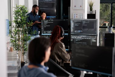Yazılım programcıları büyük ekrandaki ve dizüstü bilgisayardaki algoritmaları tartışıyorlar, html kod dilini analiz ediyorlar. Sistem mühendisleri, terminal penceresi ve sunucu arayüzündeki veritabanına bakıyor..