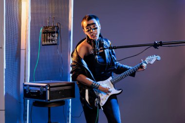 Alternatif rock gitaristi stüdyoda canlı performans sergiliyor, koyu ışıklar ve dumanla, elektro gitar çalıyor ve heaby metal şarkı söylüyor. Enstitü ve mikrofonla müzik yapmak, eğlence sanatçısı.