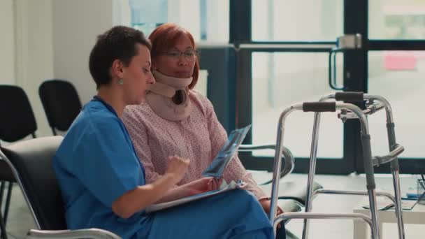 子宮頸部の襟を持つアジアの女性は X線スキャンの結果を見て 看護師からのサポートを受けて 首のフォームブレースを着用して負傷患者に放射線診断を説明アシスタント — ストック動画