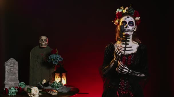 スタジオでサンタ マエルテのボディアートを身に着けている薄汚い女性は 死んだメキシコのハロウィンのお祝いの日に魅力的な演技 儀式的な頭蓋骨のボディアート 黒いバラと花冠をポーズ — ストック動画