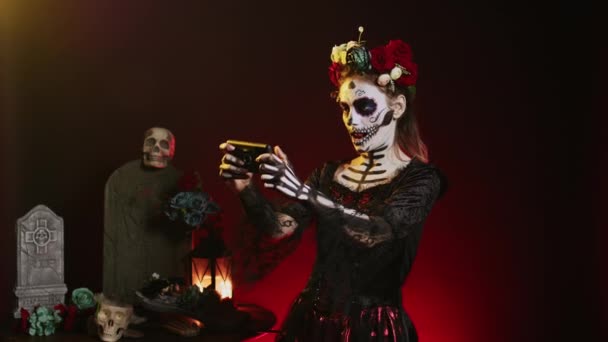 死んだお祝いの日にオンライン携帯電話を使用して スマートフォンでビデオゲームをプレイラ カヴァレラカトリーナモデル 聖メキシコ祭り 不気味な休日で楽しい時間を過ごしているサンタ マウテ — ストック動画