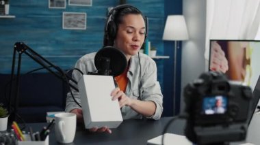 Creative tech enthusiast recording unboxing video with professional camera while presenting device specifications to audience. Digital content creator unpacking promoted product while doing review.