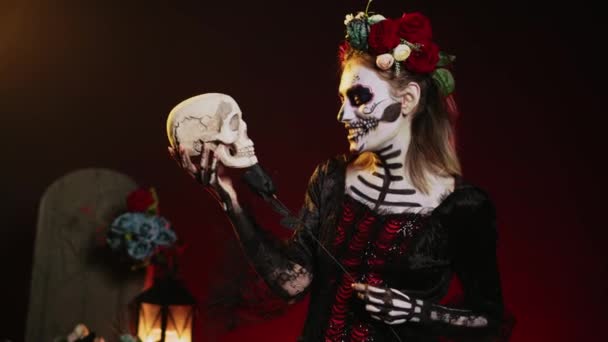 ホラー女性モデルは メキシコの休日を祝うために伝統的なボディアートを身に着けて 頭蓋骨や黒いバラと浮気を演技 ディオス ムエルトスの儀式で死の女神のように見える 手持ち撮影 — ストック動画