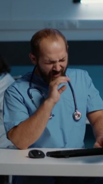 Dikey video: Hastane ofisinde saatlerce çalışan yorgun doktor hemşire hasta raporunu bilgisayarda yazıyor. İlaç reçetesini inceleyen asistan. Sağlık hizmetleri