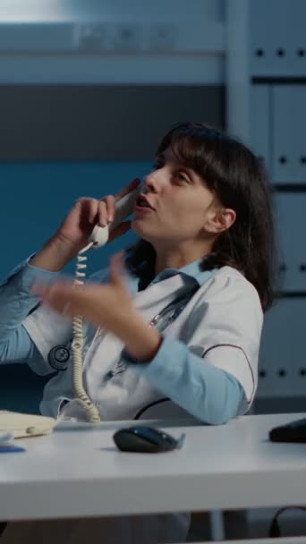 垂直视频 在医院办公室上夜班时 松驰的医生脚坐在桌子上 与远方的朋友通电话 从事医学报告分析工作的医生妇女 — 图库视频影像