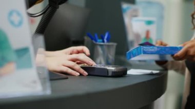 Afro-Amerikalı biri eczane tezgahında ilaç almak için kredi kartıyla ilaç ödüyor. Müşteri temassız ödeme yapıyor, takviye malzemeler alıyor. Kapatın. El kamerasıyla..