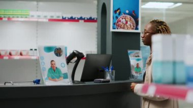 Afro-Amerikalı bir kadın eczane tezgahında ilaç almak için kredi kartıyla ilaç ödüyor. Müşteri temas kurmadan ödeme yapıyor ve ilaç alıyor..