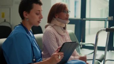 Boyunluğu ve yürüyüş çerçevesi olan hemşire danışmanı bir hasta. Tablete kaza yaralanması hakkında notlar alıyor. Rahim ağzı köpüğü ve sakatlığı olan bir kadınla check-up yapıyorum..